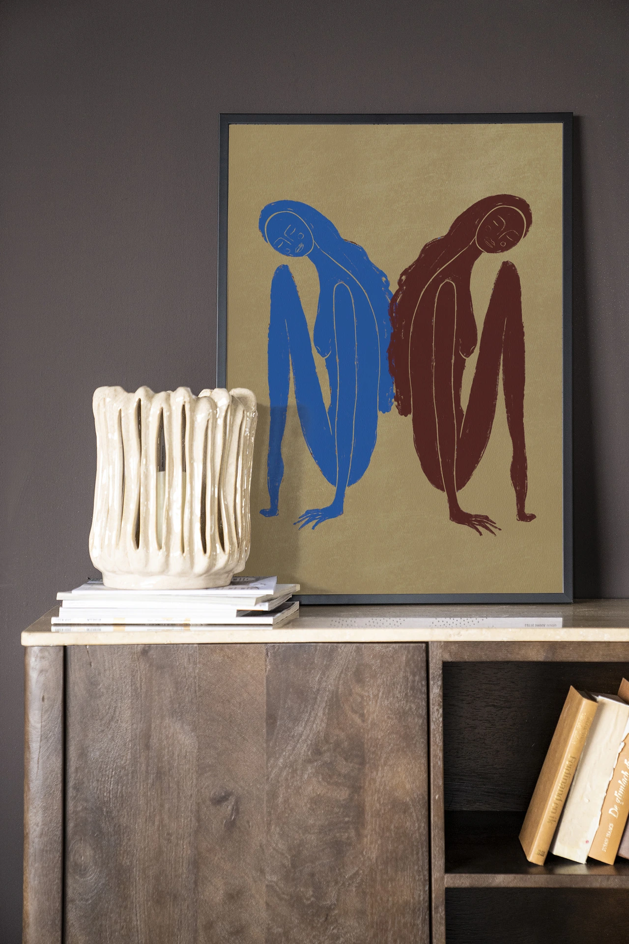Wandkleed Sync Motion - Urban Cotton hangend boven een houten dressoir met boeken en een vaas