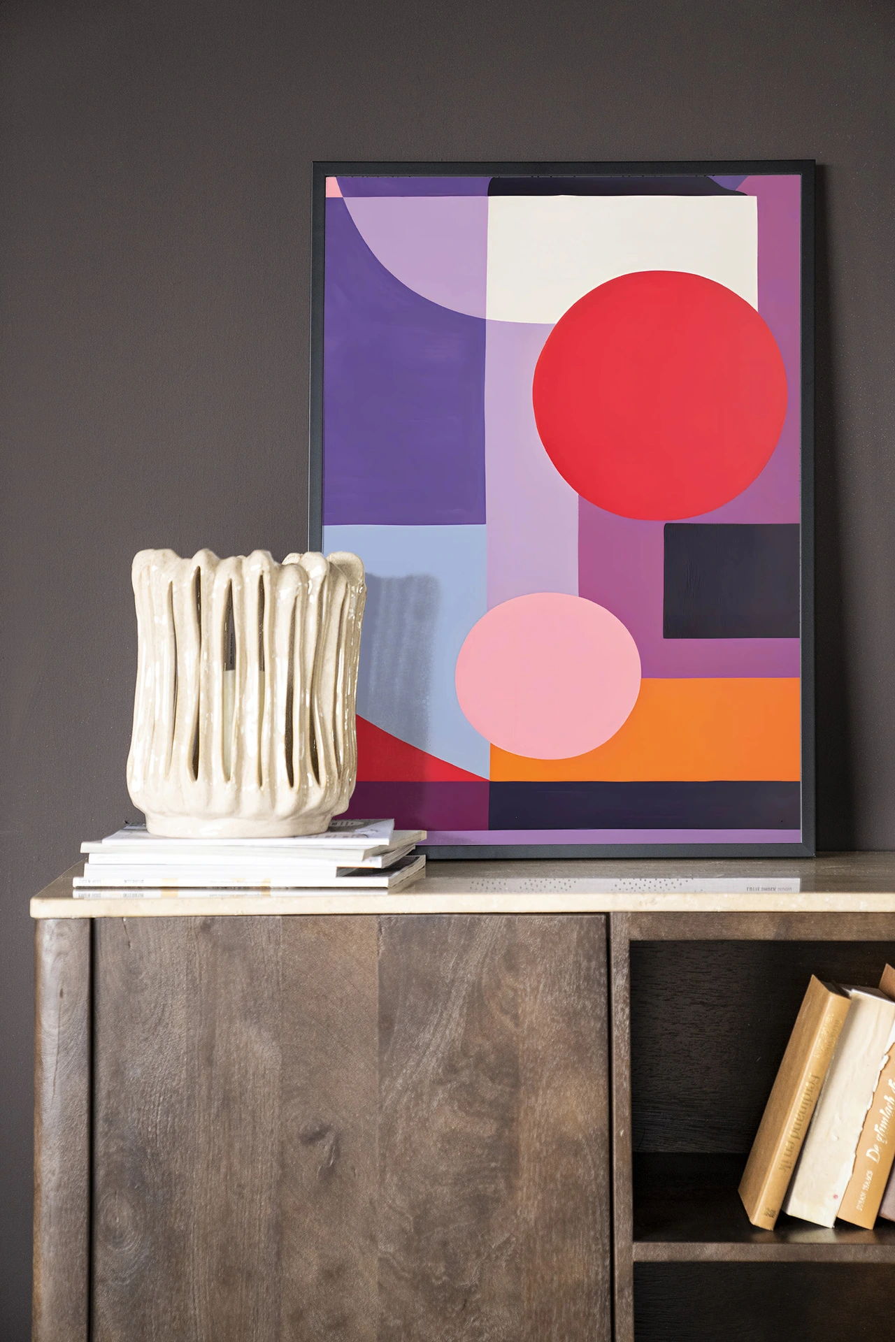 Wandkleed Attraction van Urban Cotton in een lijst, staand op een houten dressoir met boeken