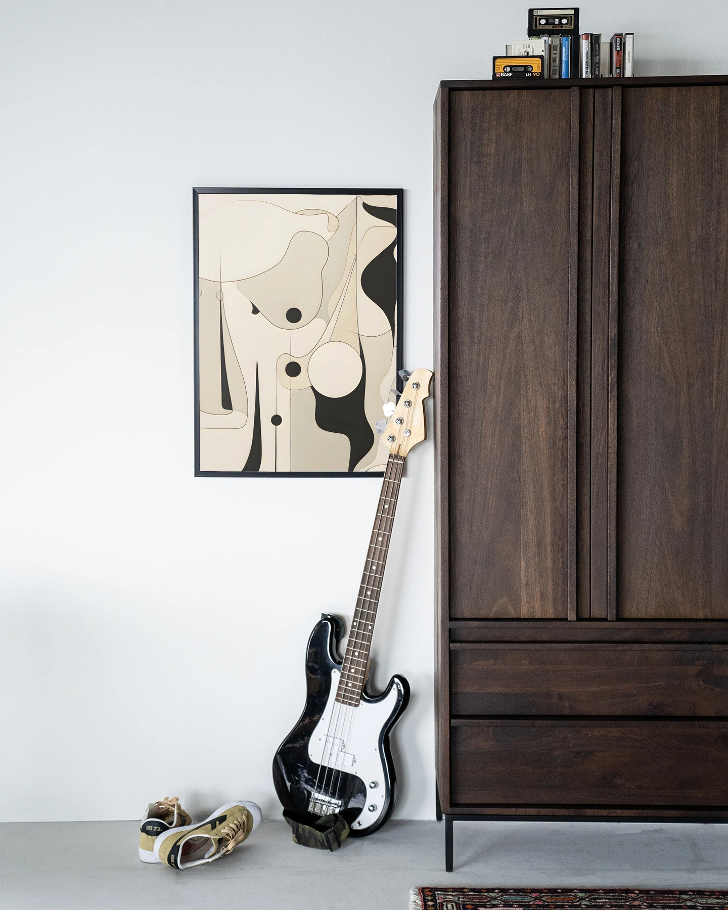 De Art print Rocamadour - Urban Cotton hangt aan een witte muur naast een donkerbruine kast met een basgitaar ervoor