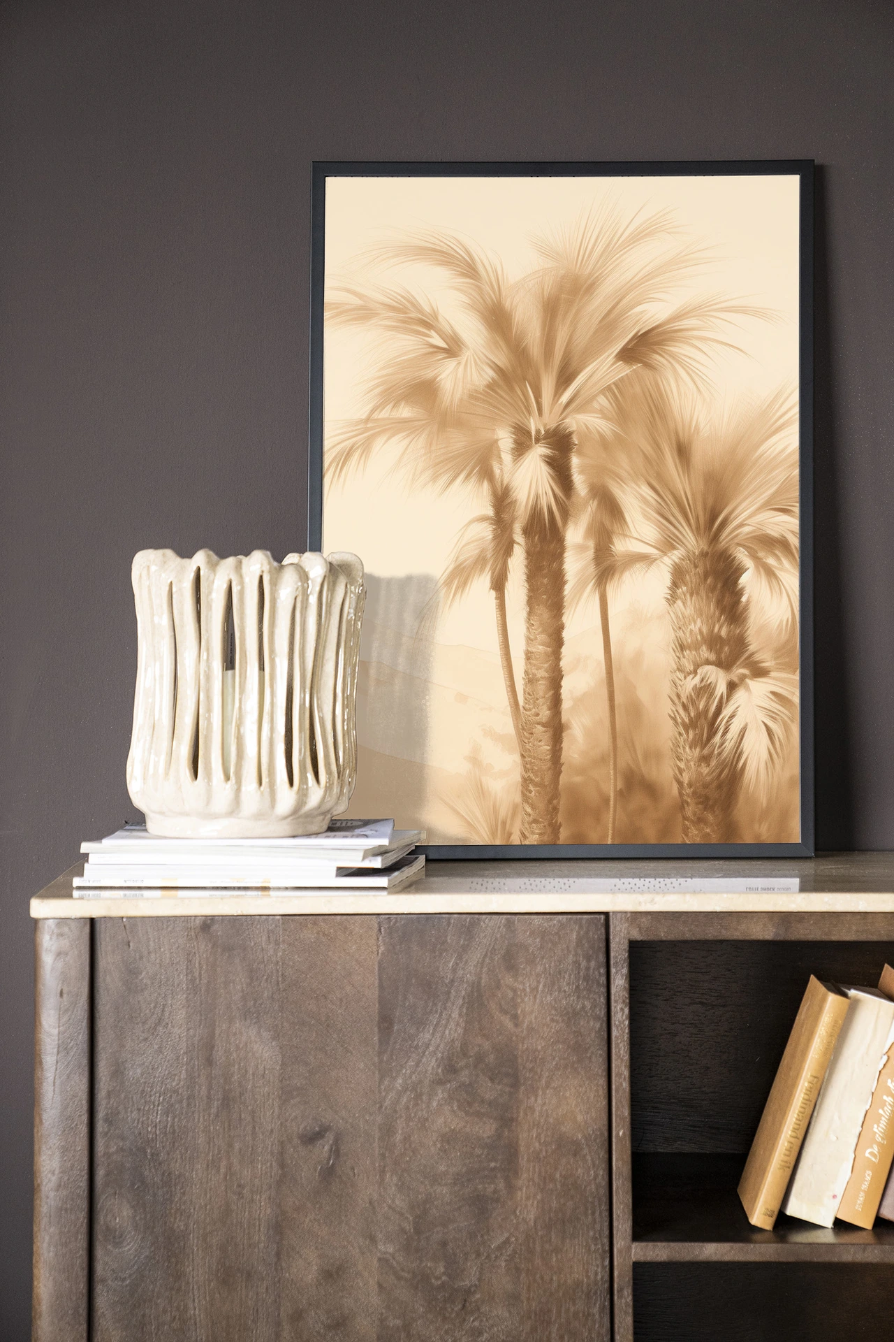 Wandkleed Desert Mirage - Urban Cotton in een lijst, staand op een houten dressoir met boeken en een vaas
