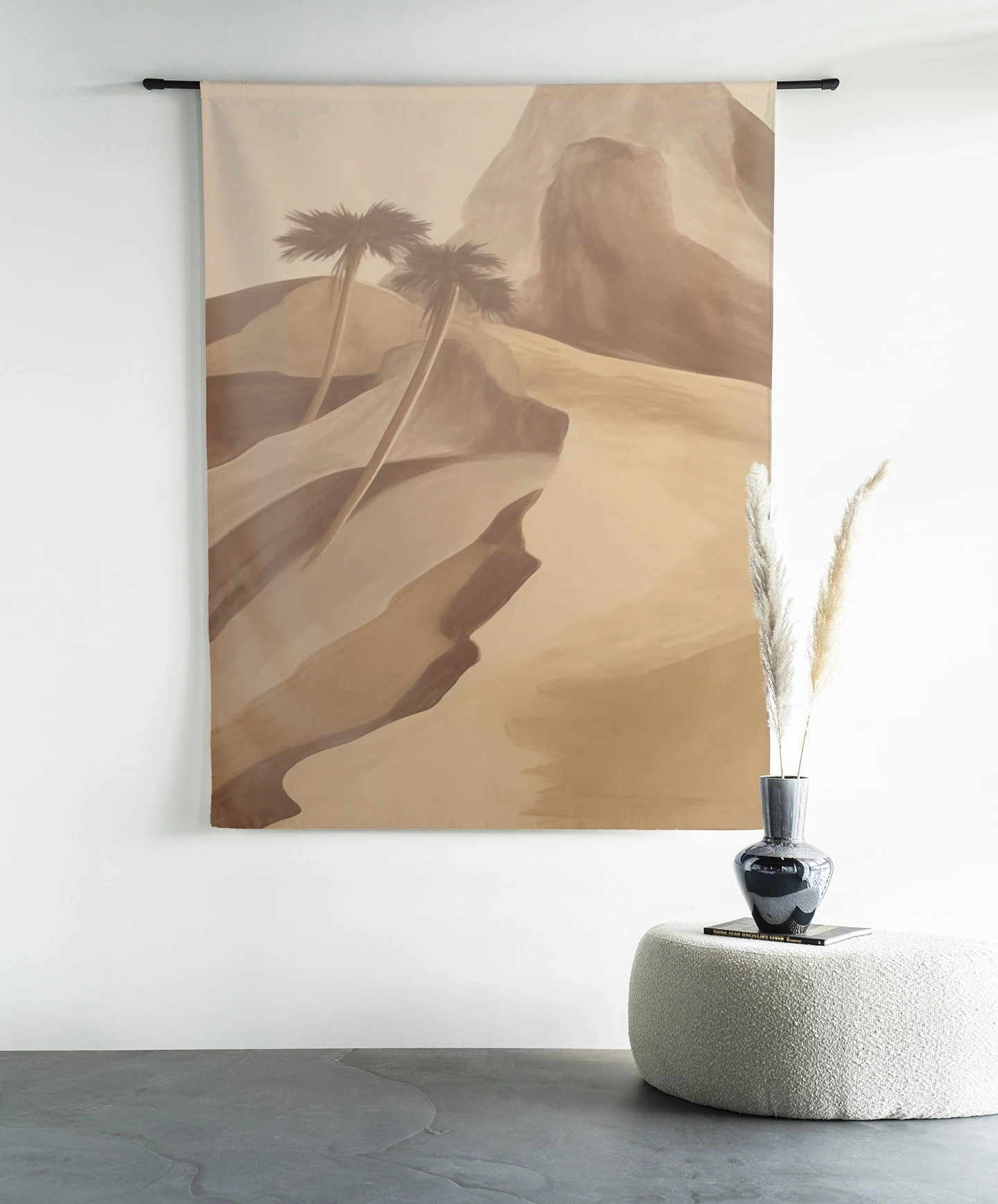 Een wandkleed met woestijnlandschap en palmbomen hangt aan een zwarte roede boven een poef met vaas - Urban Cotton