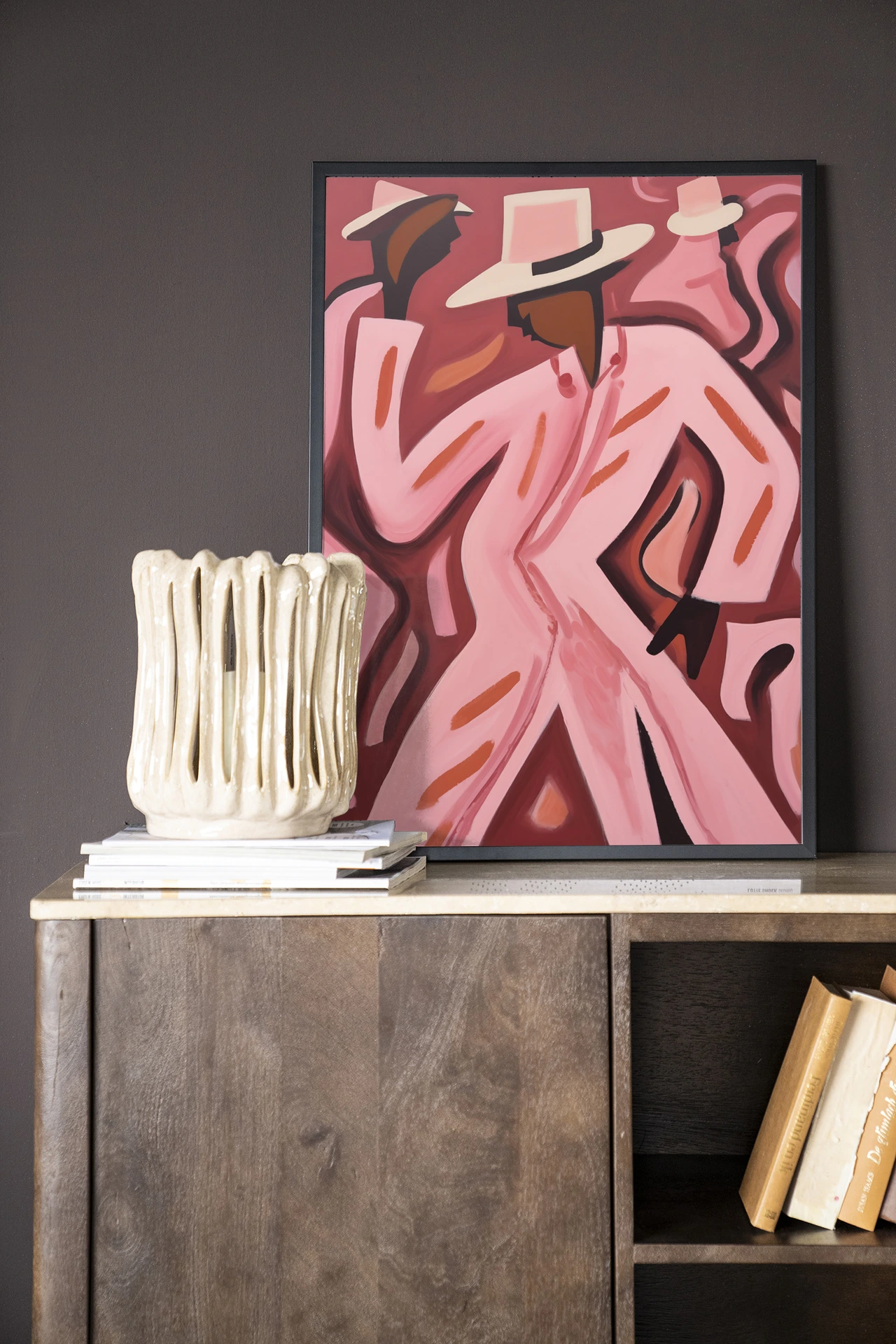 Een Wandkleed Boogie Woogie - Urban Cotton in een zwarte lijst, leunend op een houten dressoir met een vaas en boeken