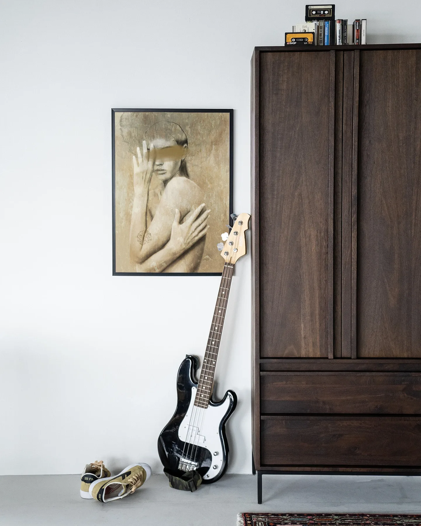 Wandkleed Touching Me - Urban Cotton hangend aan een witte muur boven een basgitaar en schoenen