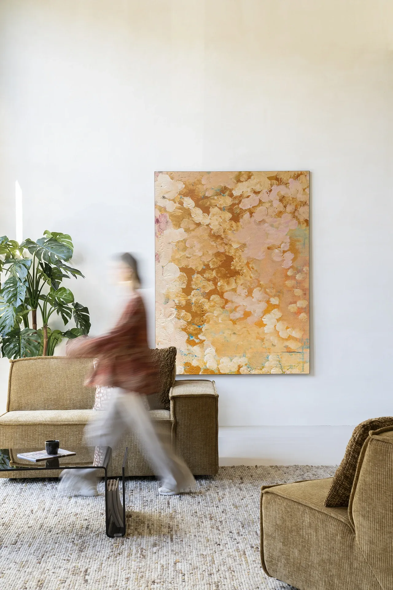 Wandteppich Abundance - Urban Cotton hängt an einer weißen Wand in einem Wohnzimmer mit einem Sofa und einer vorbeigehenden Person
