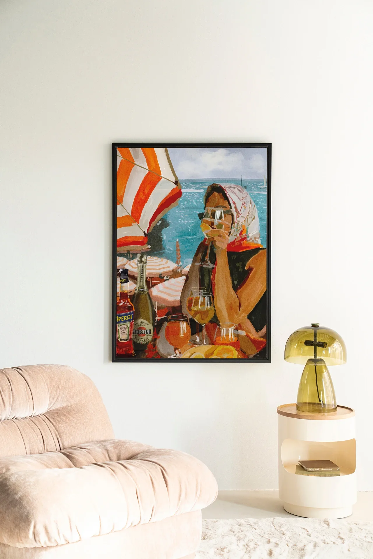 Wandteppich Aperol o'clock - Urban Cotton hängt an einer weißen Wand neben einem beigefarbenen Sessel und einem Nachttisch