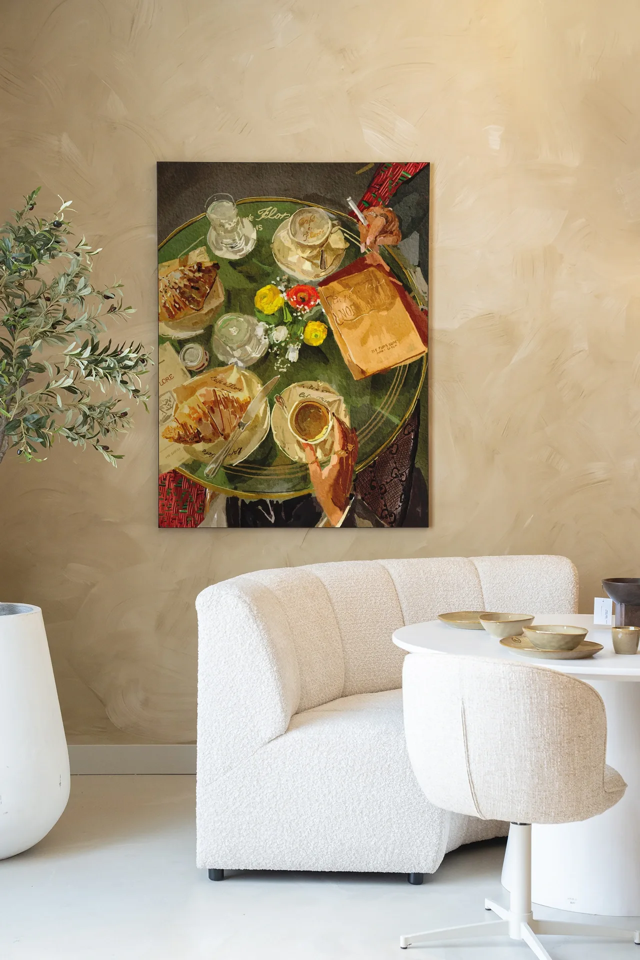 Ein Wandteppich mit einer Illustration von Croissants und Kaffee auf einem Tisch, der über einem beigen Sofa und einem weißen Tisch in einem hellen Raum hängt - Urban Cotton