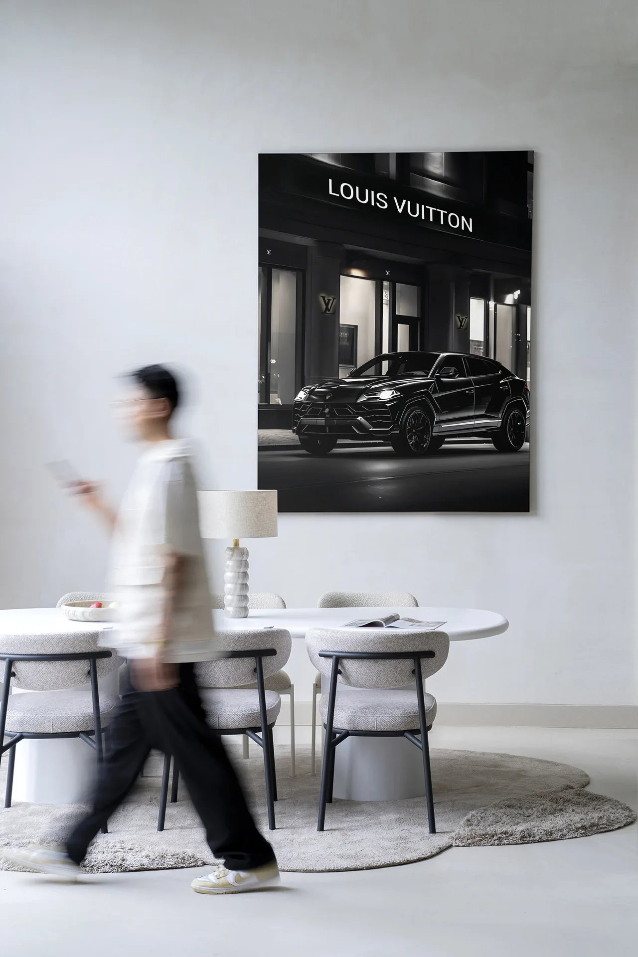 Eine verschwommene Person geht an einem weißen Tisch mit Stühlen und einem Wandteppich Urus LV - Urban Cotton an der Wand vorbei