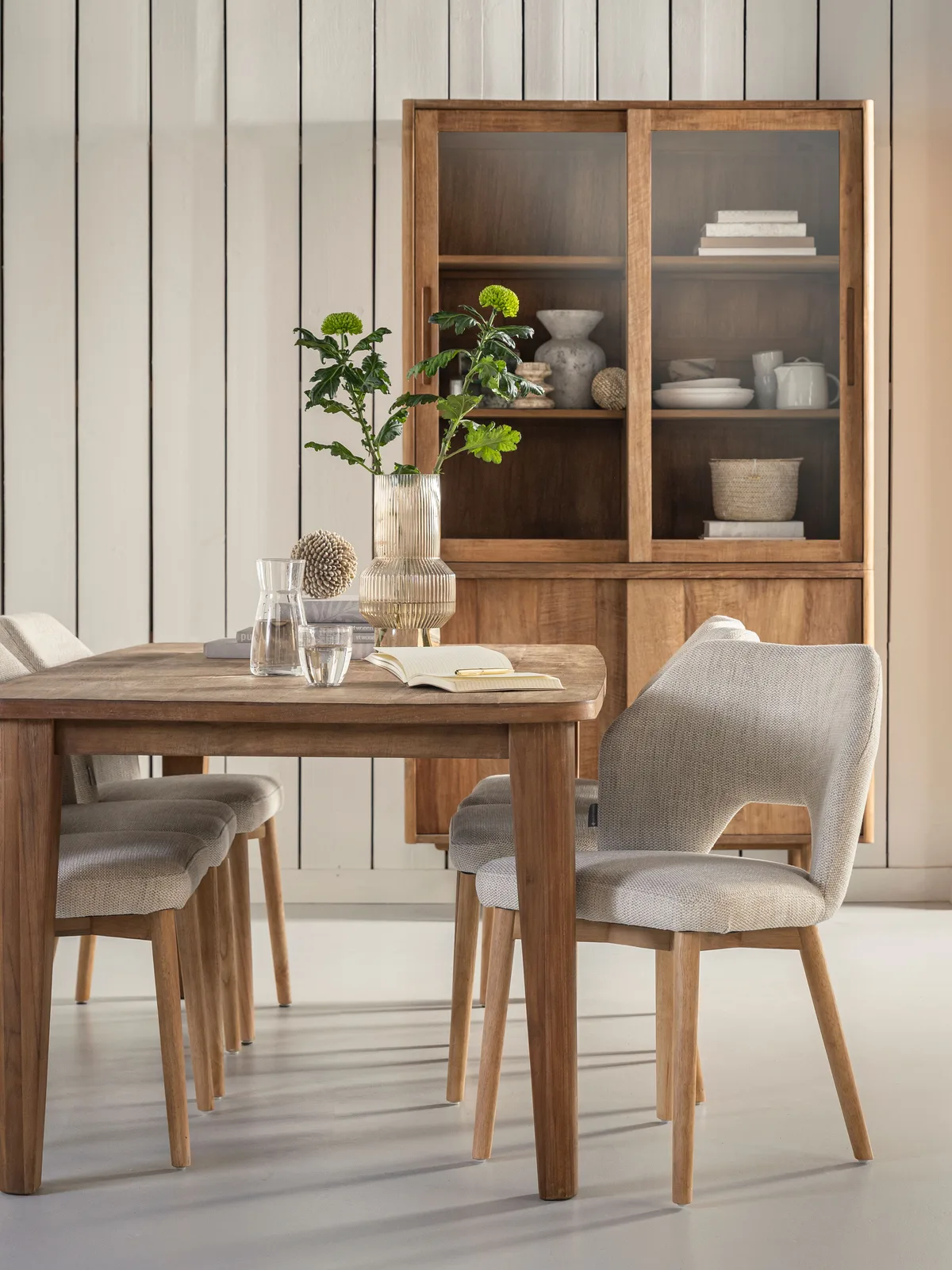 Der Vitrinenschrank Bliss mittel in einem hellen Wohnzimmer mit Esstisch und Stühlen, von der Seite gesehen - DTP Home