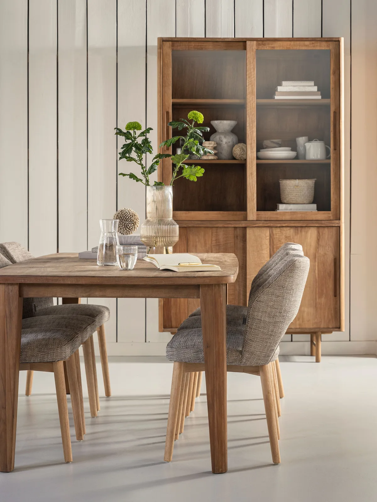 Der Vitrinenschrank Bliss mittel in einem hellen Esszimmer mit Holztisch und Stühlen, dekoriert mit Pflanzen und Geschirr - DTP Home