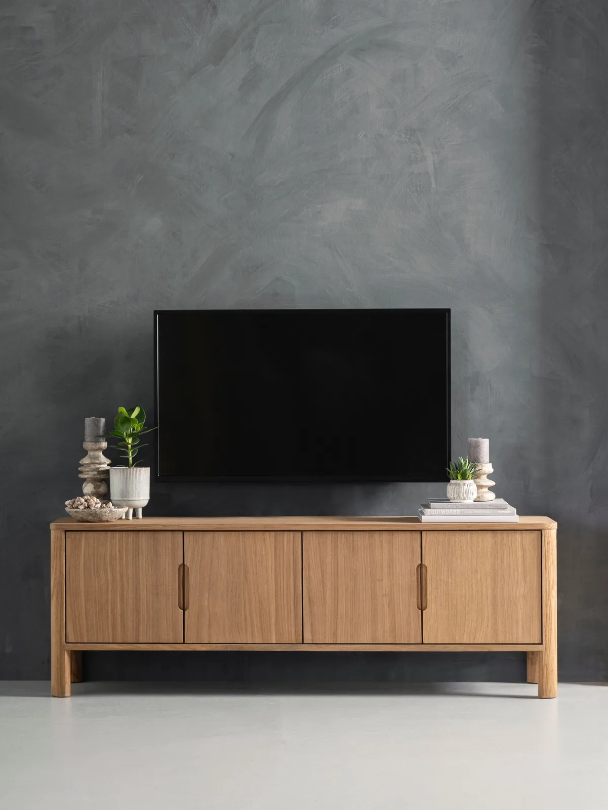 Tv-Möbel Forte in einer Studio-Umgebung mit Accessoires und einem Fernseher an einer dunkelgrauen Wand - DTP Home