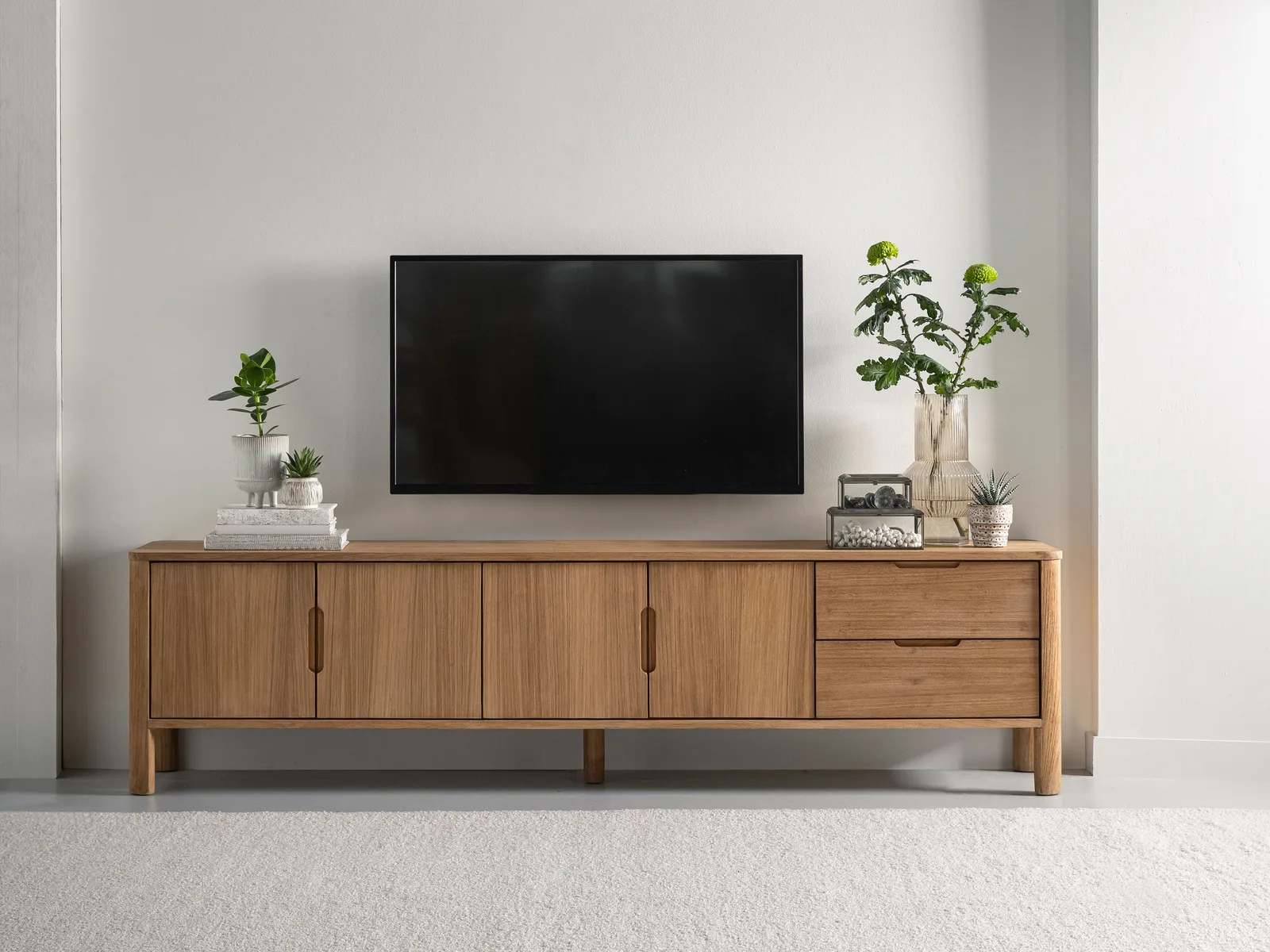 Tv-Möbel Forte in einem hellen Wohnzimmer, mit einem Fernseher darüber und Dekoration darauf - DTP Home