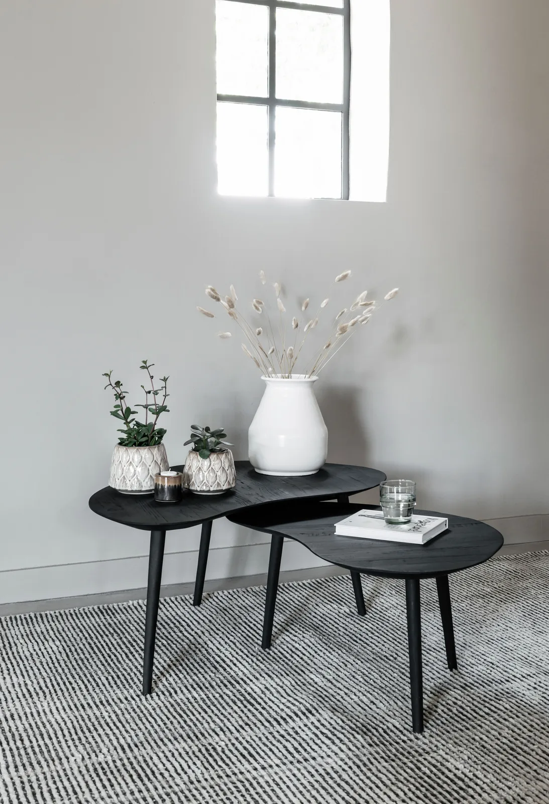 Drie zwarte Salontafel Organus tafels in een woonkamer met een wit vloerkleed en planten - DTP Home