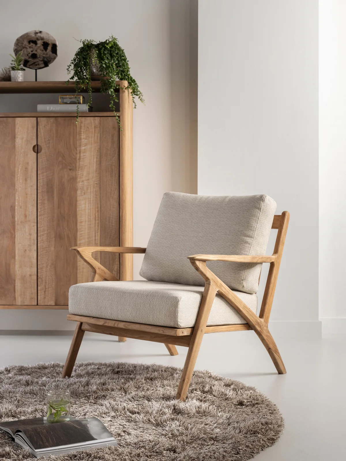 Loungesessel Charles in einem hellen Wohnzimmer mit einem Holzschrank und einem runden Teppich - MUST Living