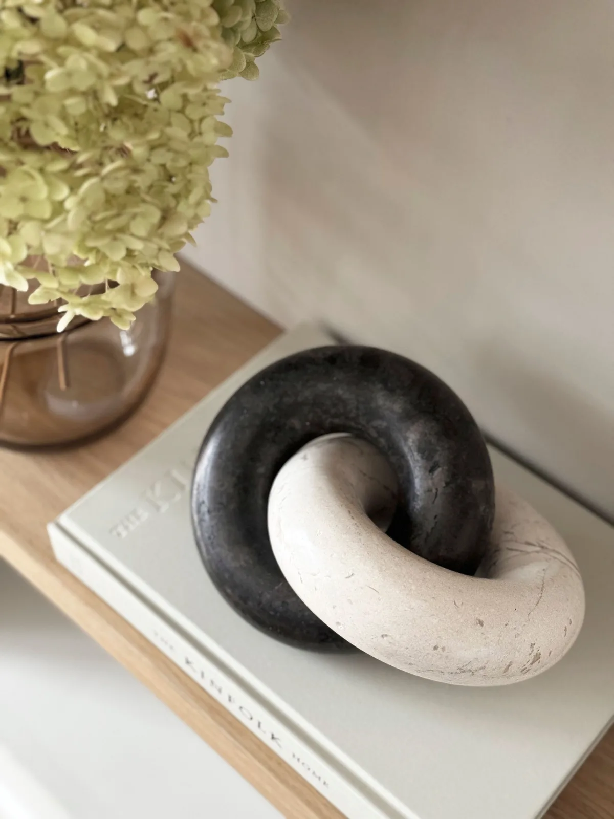 Een close-up van twee in elkaar grijpende decoratieve ringen, een zwarte en een witte, op een boek - MUST Living