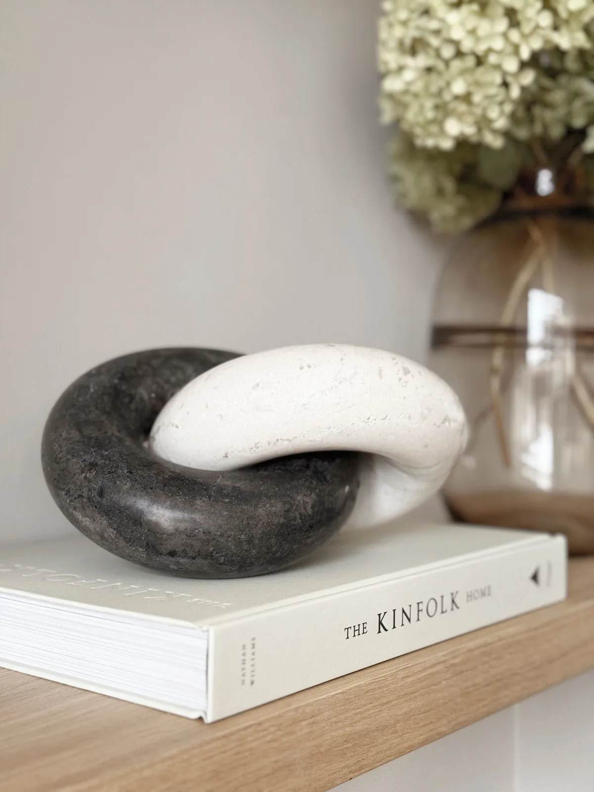 Een decoratief object met in elkaar grijpende zwarte en witte schakels, liggend op een boek op een houten plank - MUST Living