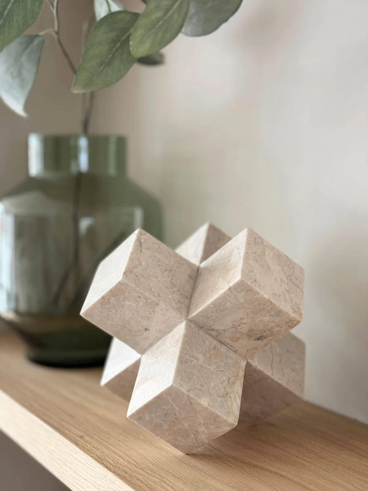 Een decoratief object in de vorm van een ster op een houten plank, met een groene vaas en plant op de achtergrond - MUST Living