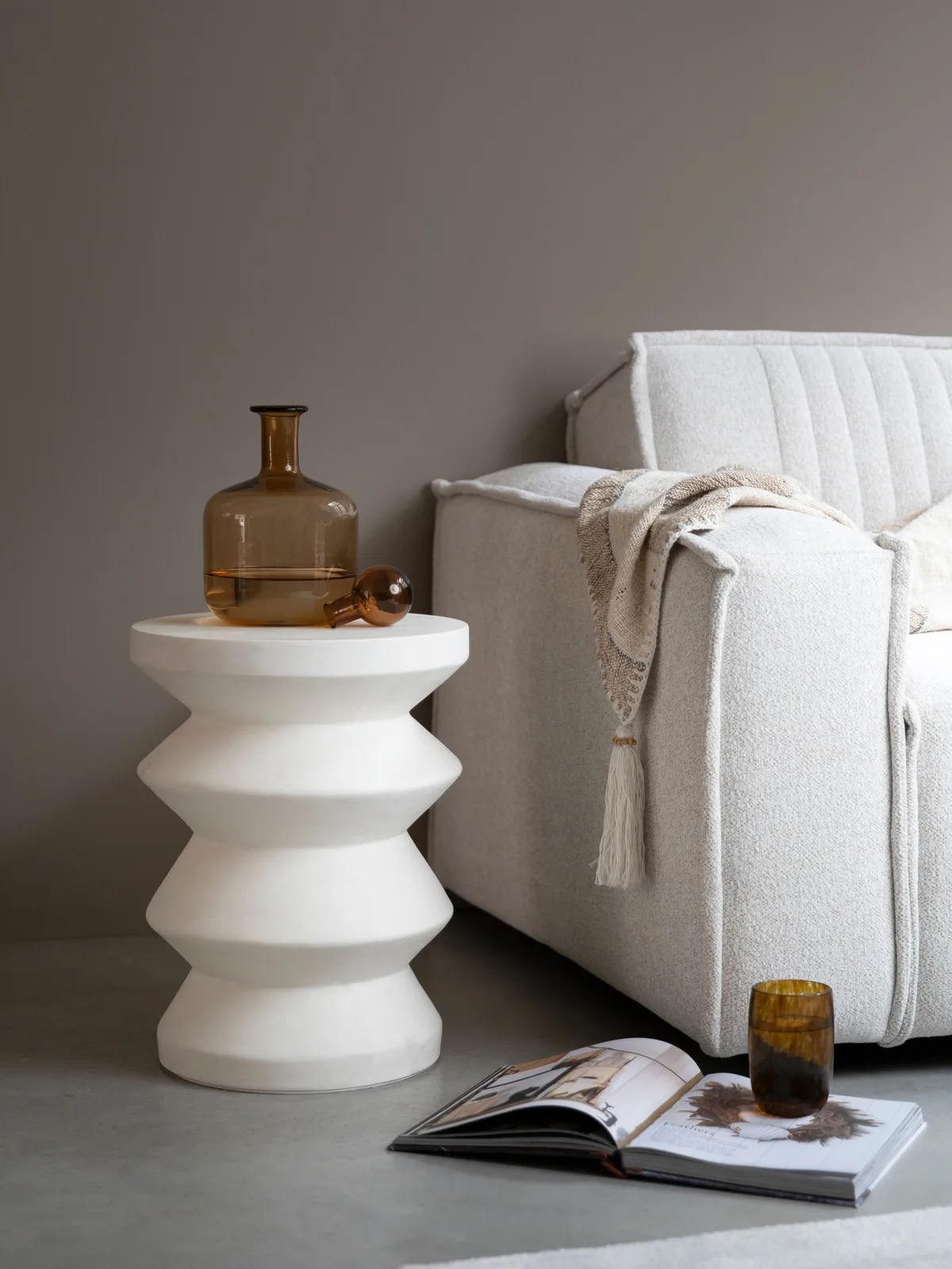 Der weiße Beistelltisch Zig Zag steht neben einem cremefarbenen Sofa, mit einer Vase und einem Glas darauf - MUST Living