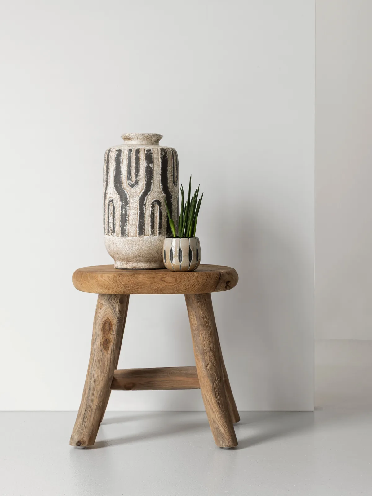 Die Vase Porto steht zusammen mit einer kleinen Pflanze auf einem Holzhocker vor einem weißen Hintergrund - MUST Living