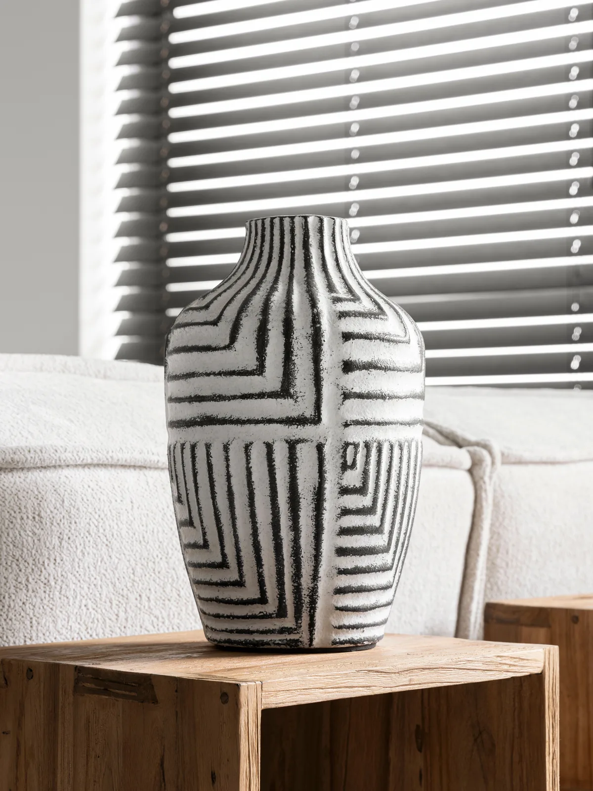 Vase Braga auf einem hölzernen Beistelltisch in einem Wohnzimmer mit Sofa und Jalousien - MUST Living