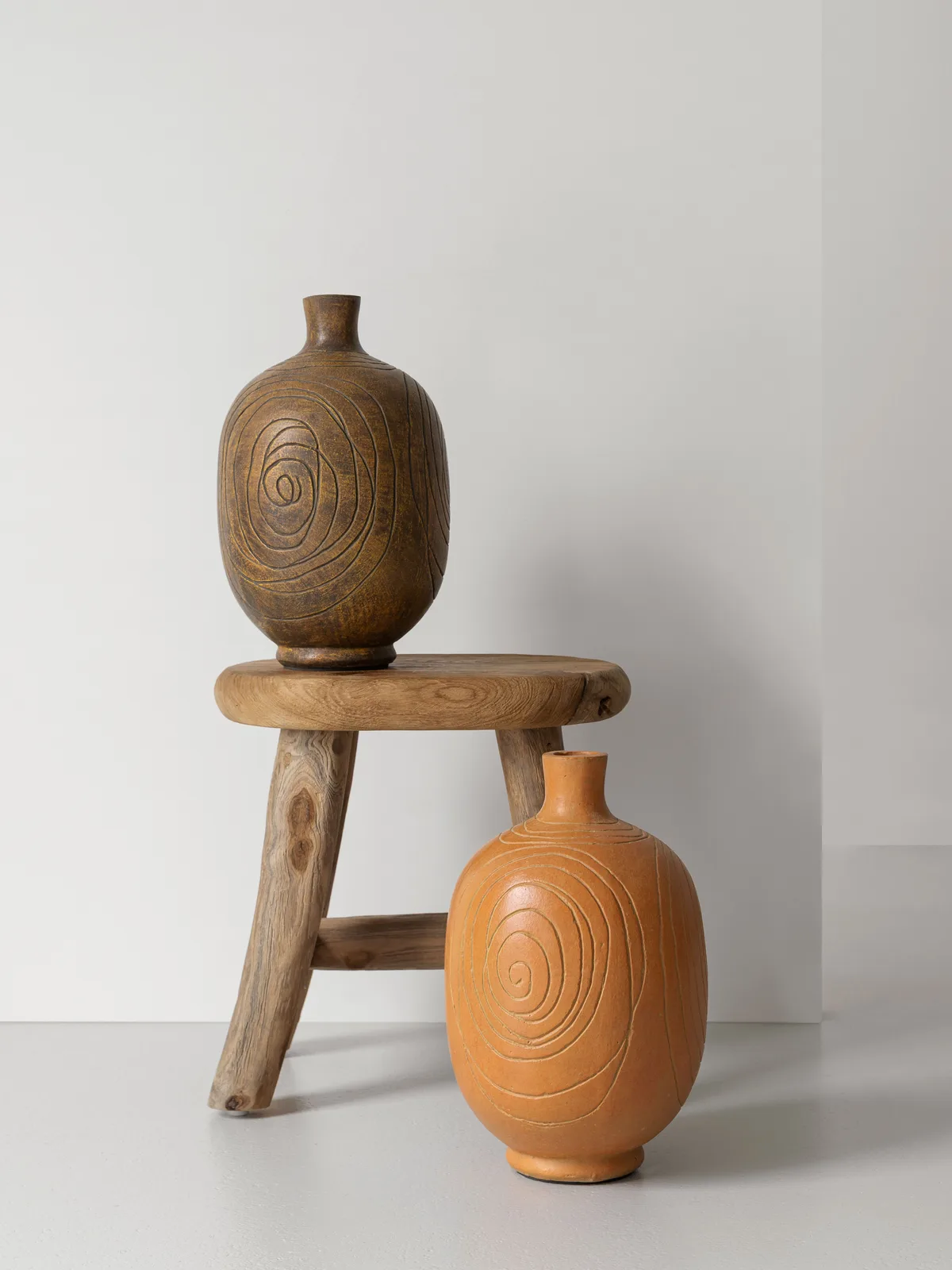Zwei Vase Lisbon Vasen mit Spiralmuster, eine dunkelbraune auf einem Holzhocker und eine orange daneben - MUST Living