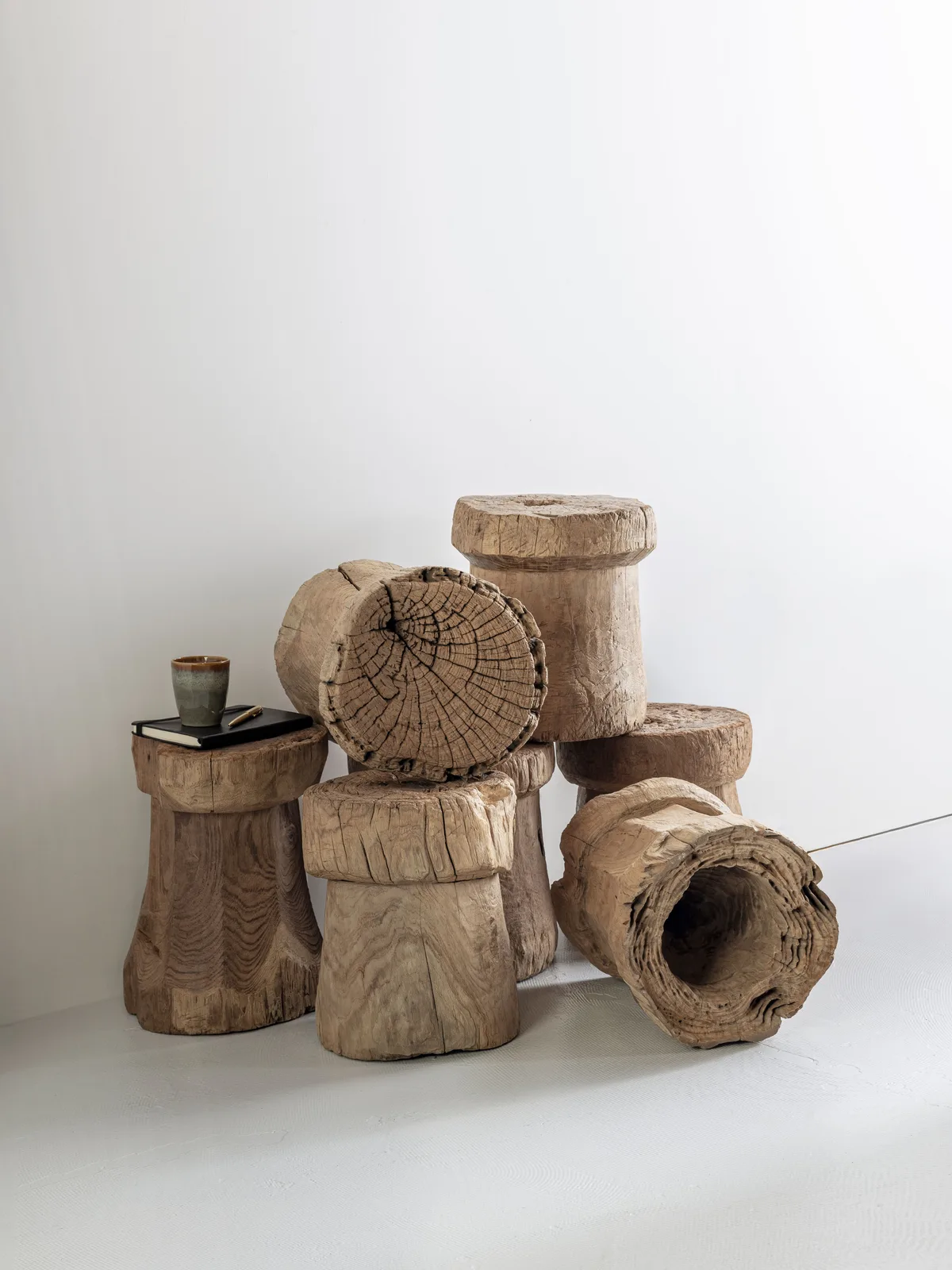 Beistelltisch Toba in einer Studio-Inszenierung mit mehreren Holzhockern und einem Notizbuch mit Tasse - MUST Living