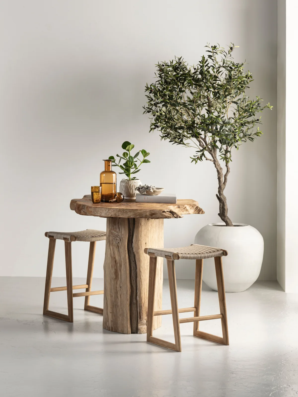 Gartentisch Merapi mit zwei Hockern in einem hellen Studio mit einem Olivenbaum - MUST Living