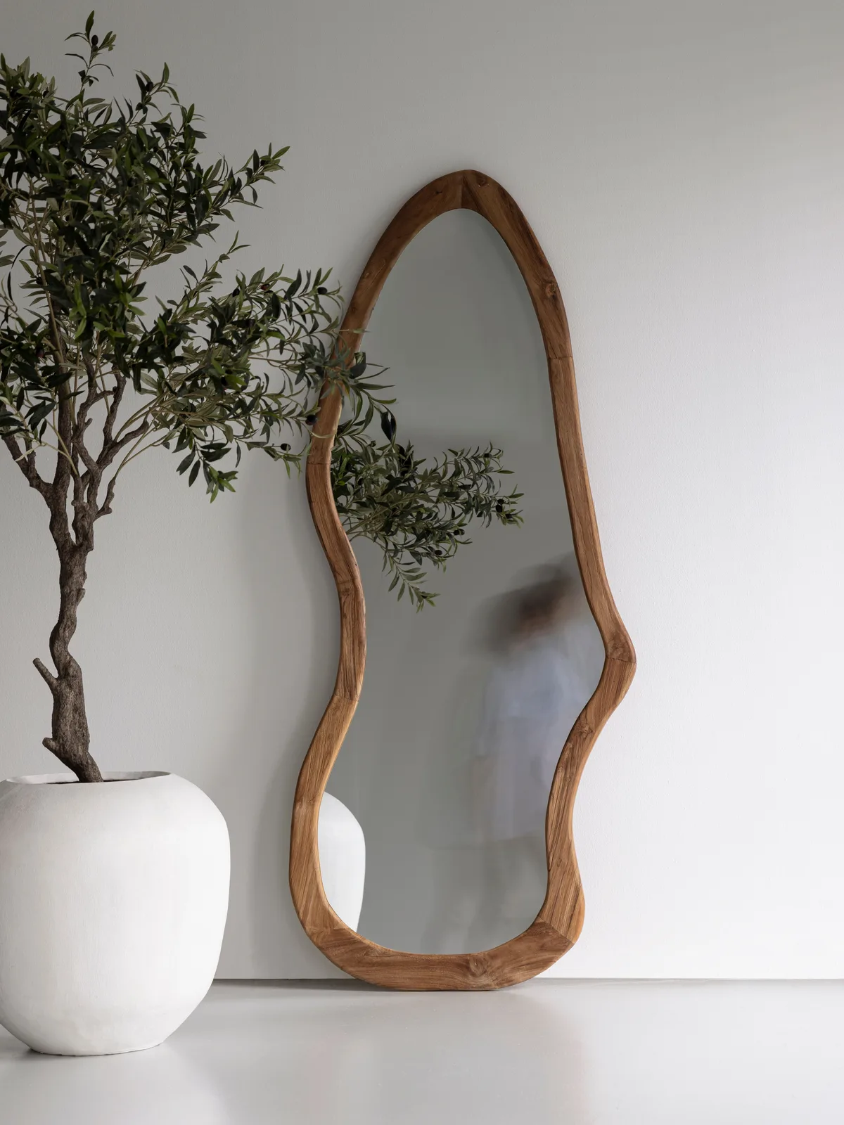 Spiegel Mirror Mateo mit organischer Form, der an einer weißen Wand neben einem Olivenbaum in einem weißen Topf steht - MUST Living