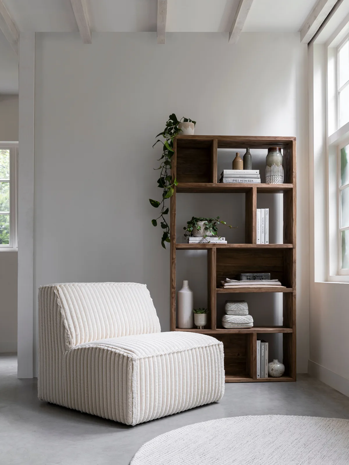 Runder weißer Teppich Asuri auf einem grauen Boden in einem hellen Wohnzimmer mit Sessel und Holzregal - MUST Living
