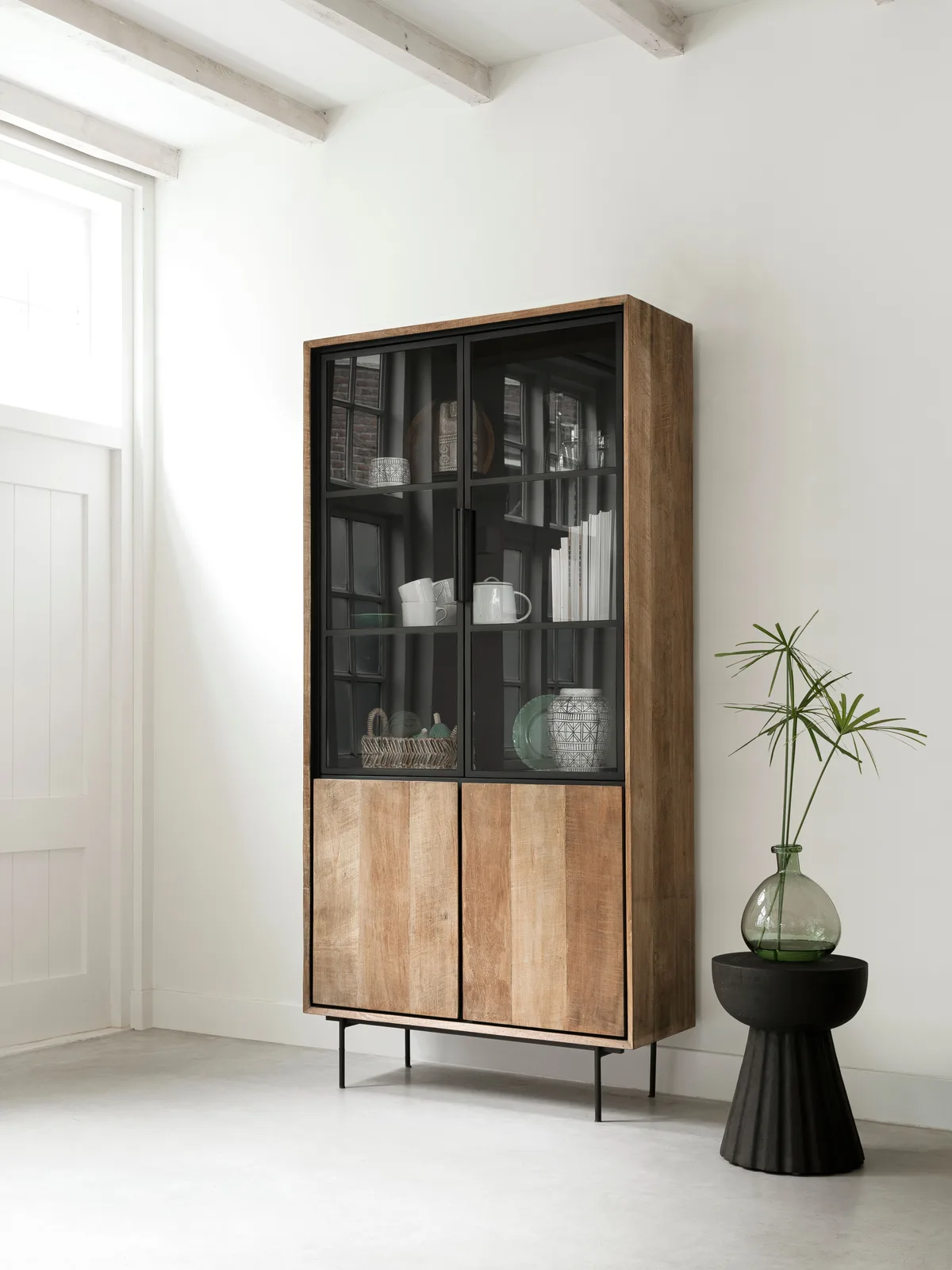 Vitrinekast Metropole in een lichte woonkamer met decoratie en een plant op een bijzettafel - DTP Home