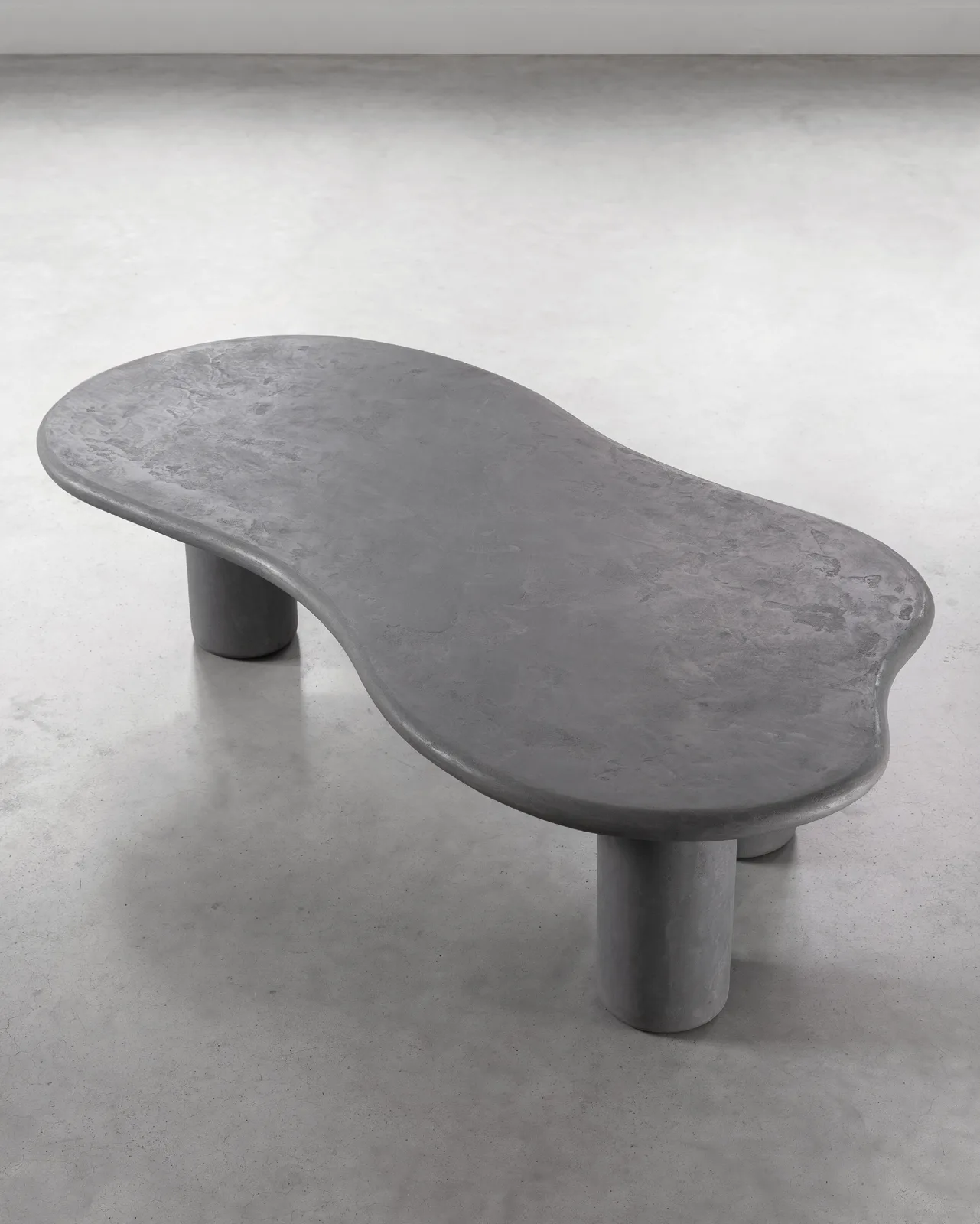 Salontafel Curva van DTP Home, een organisch gevormde grijze tafel met drie poten in een studio-opstelling
