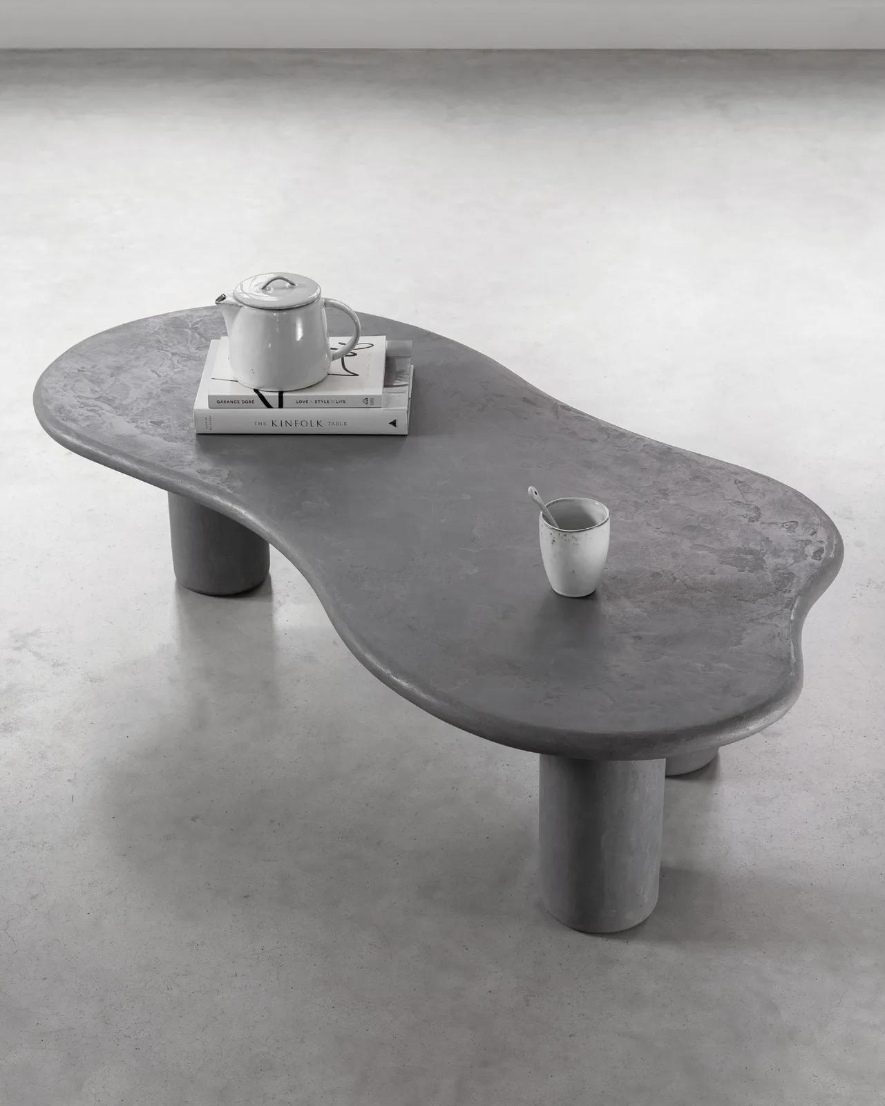 Der Couchtisch Scala Curva von DTP Home, ein organisch geformter grauer Couchtisch mit drei Beinen, in einer Studio-Umgebung