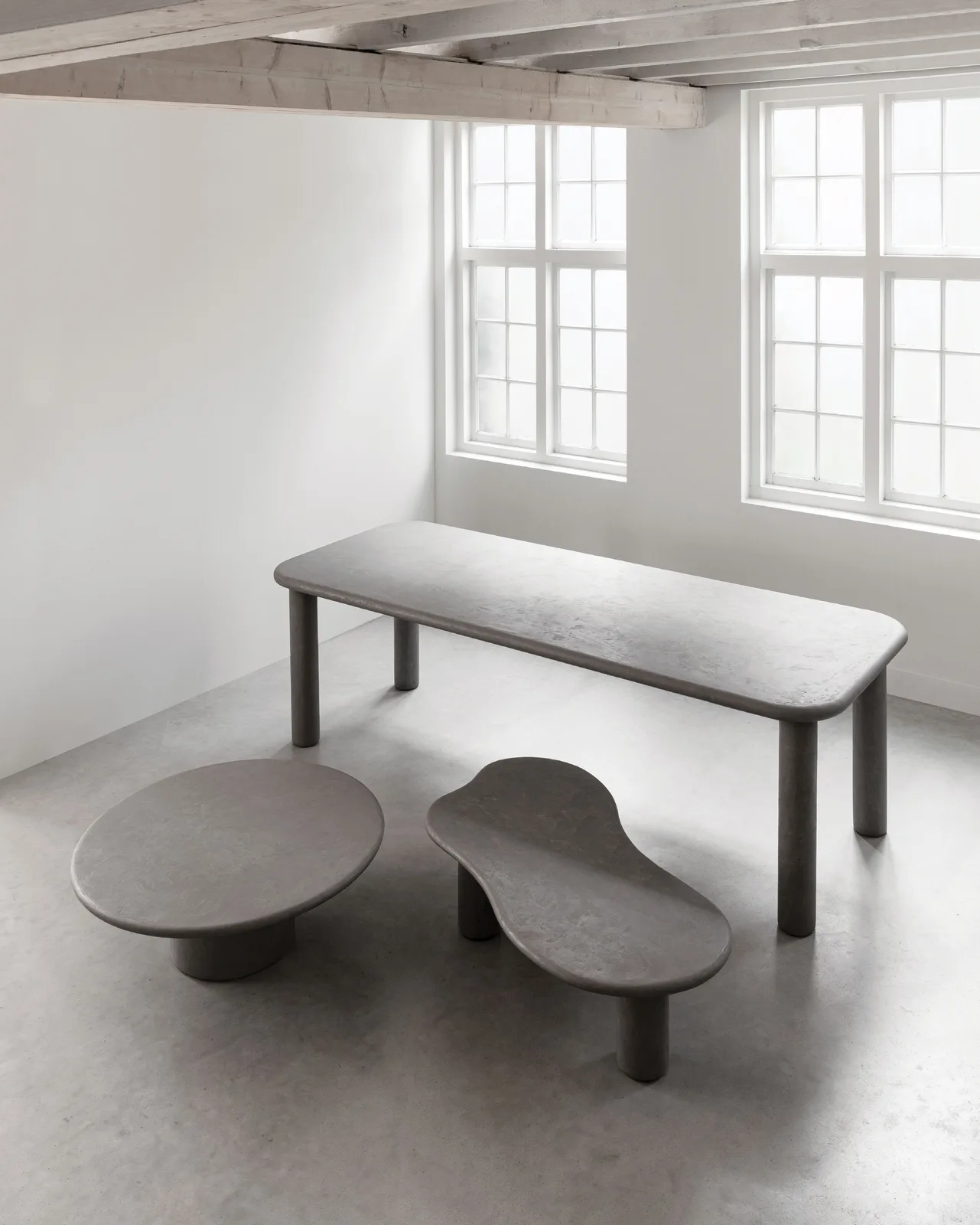 Drei graue Tische von DTP Home, darunter der Esstisch Clio, in einem minimalistischen Studio mit Fenstern