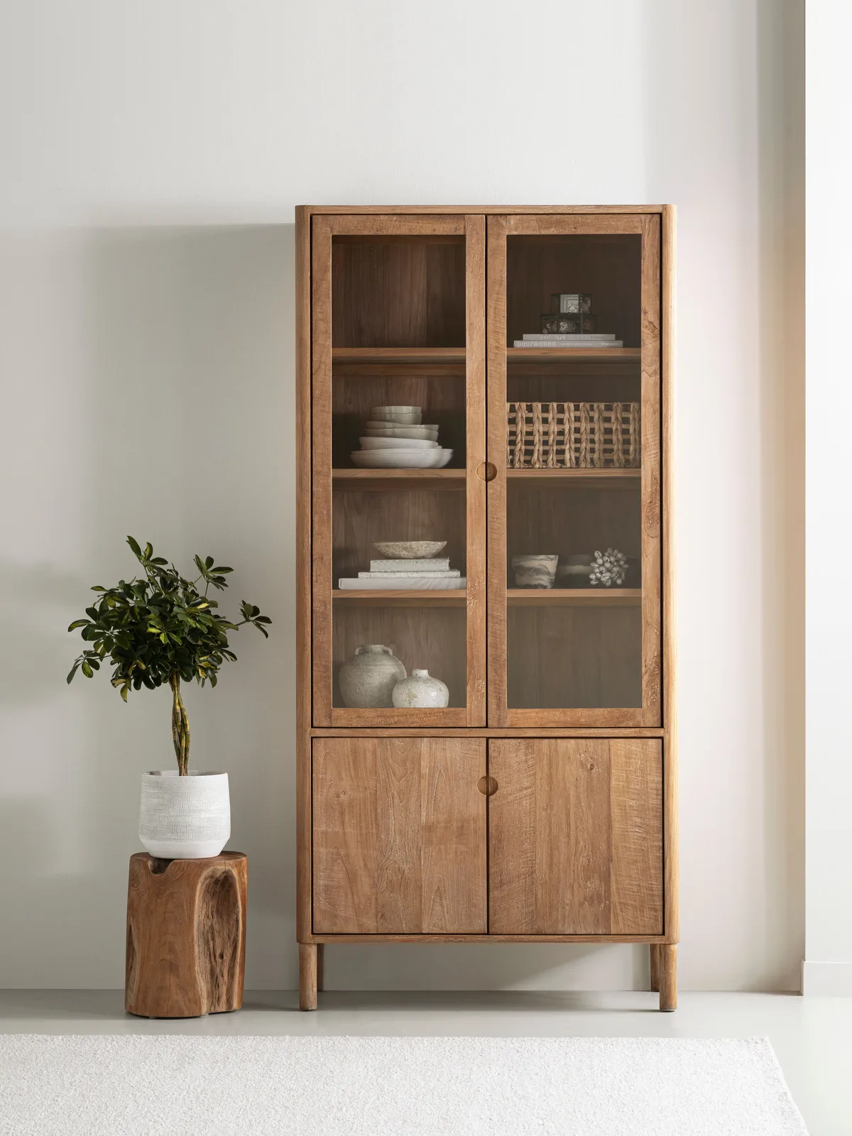 Vitrinekast Apollo in een lichte studio met een plant op een houten krukje ernaast - DTP Home