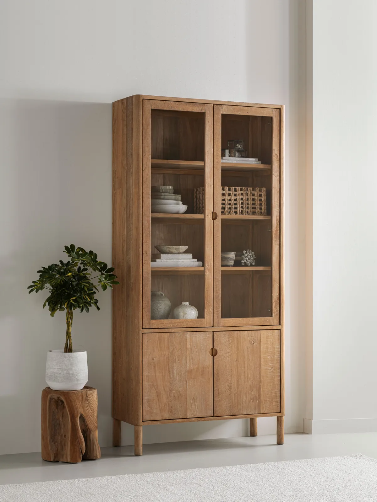 Vitrinekast Apollo in een lichte woonkamer met een plant op een houten kruk - DTP Home