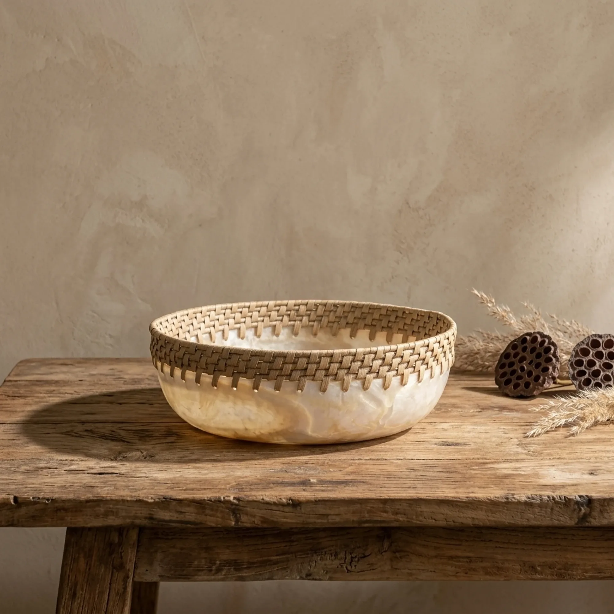 Das Tablett Bowl Da Vinci rund auf einem rustikalen Holztisch, daneben getrocknete Pflanzen und Lotuskolben - MUST Living