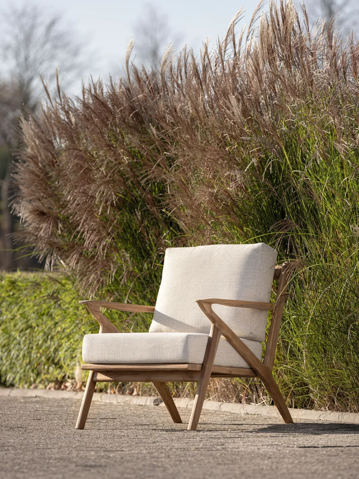 Loungesessel Charles in einem Garten mit einer hohen, flauschigen Hecke im Hintergrund - MUST Living