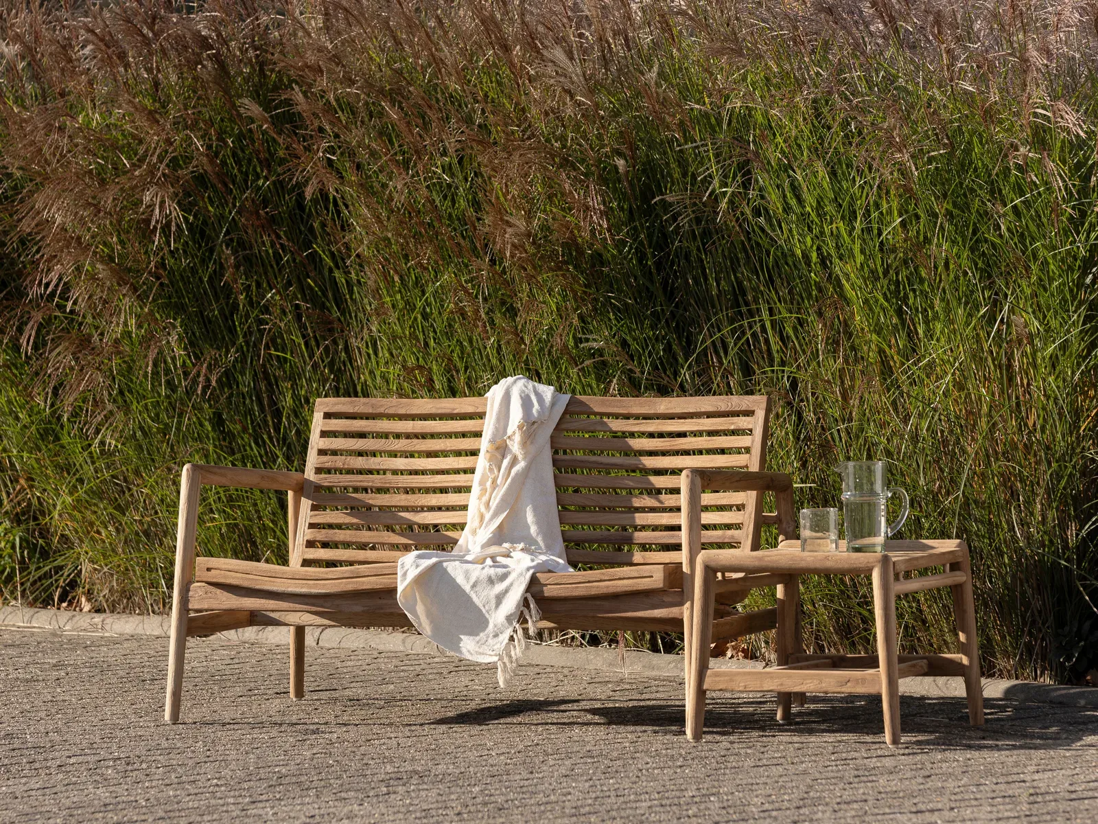Gartentisch Ray von MUST Living mit einer Bank und einem Plaid in einem Garten mit hohem Gras
