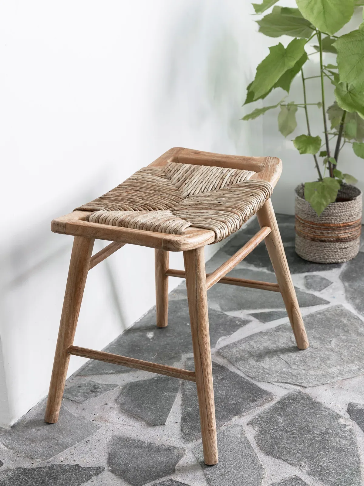 Kruk Rex met geweven zitting in een lichte studio met plant en stenen vloer - MUST Living