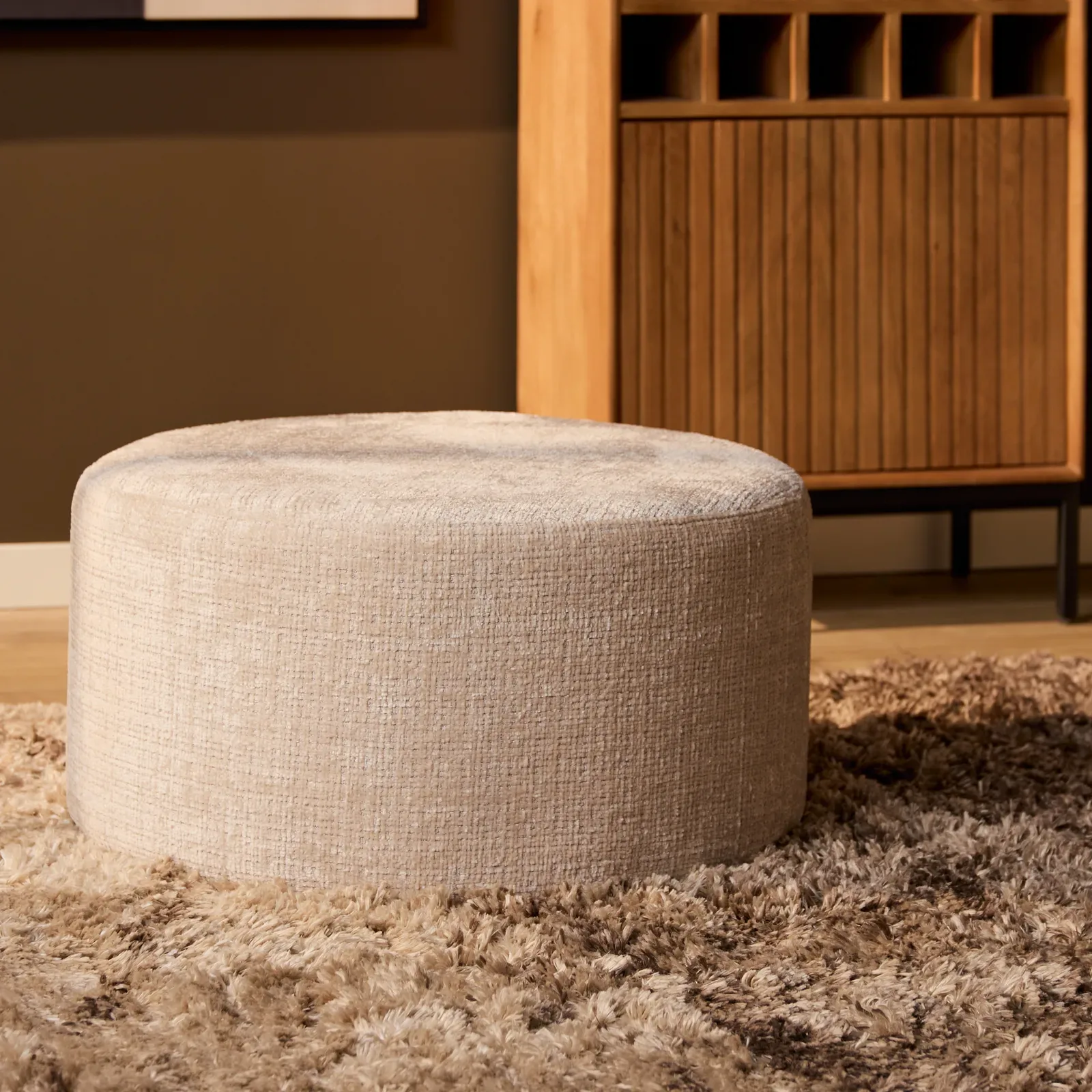 Der MySofa Runde Hocker in einem stimmungsvollen Wohnzimmer mit braunem Teppich und Holzschrank