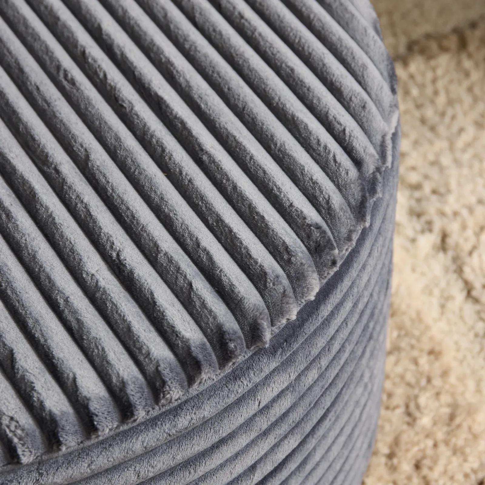 Detail des MySofa Runder Hocker mit geripptem Stoff und einem hellen Teppich im Hintergrund