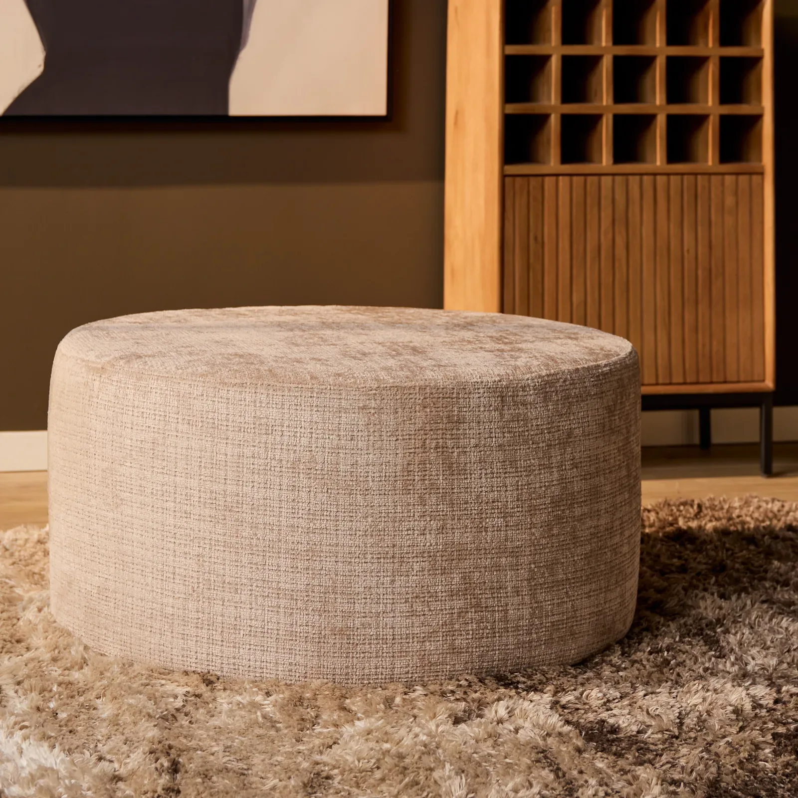 Der MySofa Runder Hocker in einem Wohnzimmer, mit einem Holzschrank und Gemälde im Hintergrund