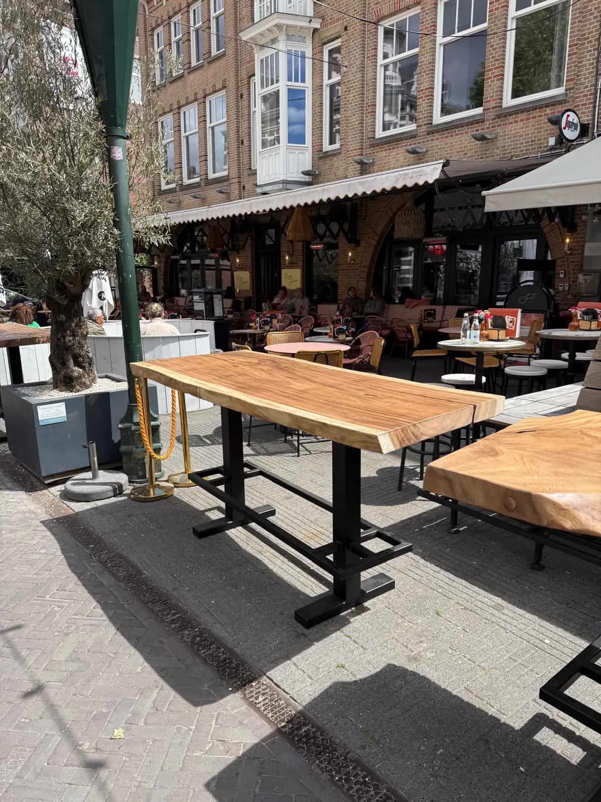 Bartisch aus Suarholz Baumstamm auf einer Terrasse mit anderen Tischen und Stühlen, von der Seite gesehen - World of Brosi
