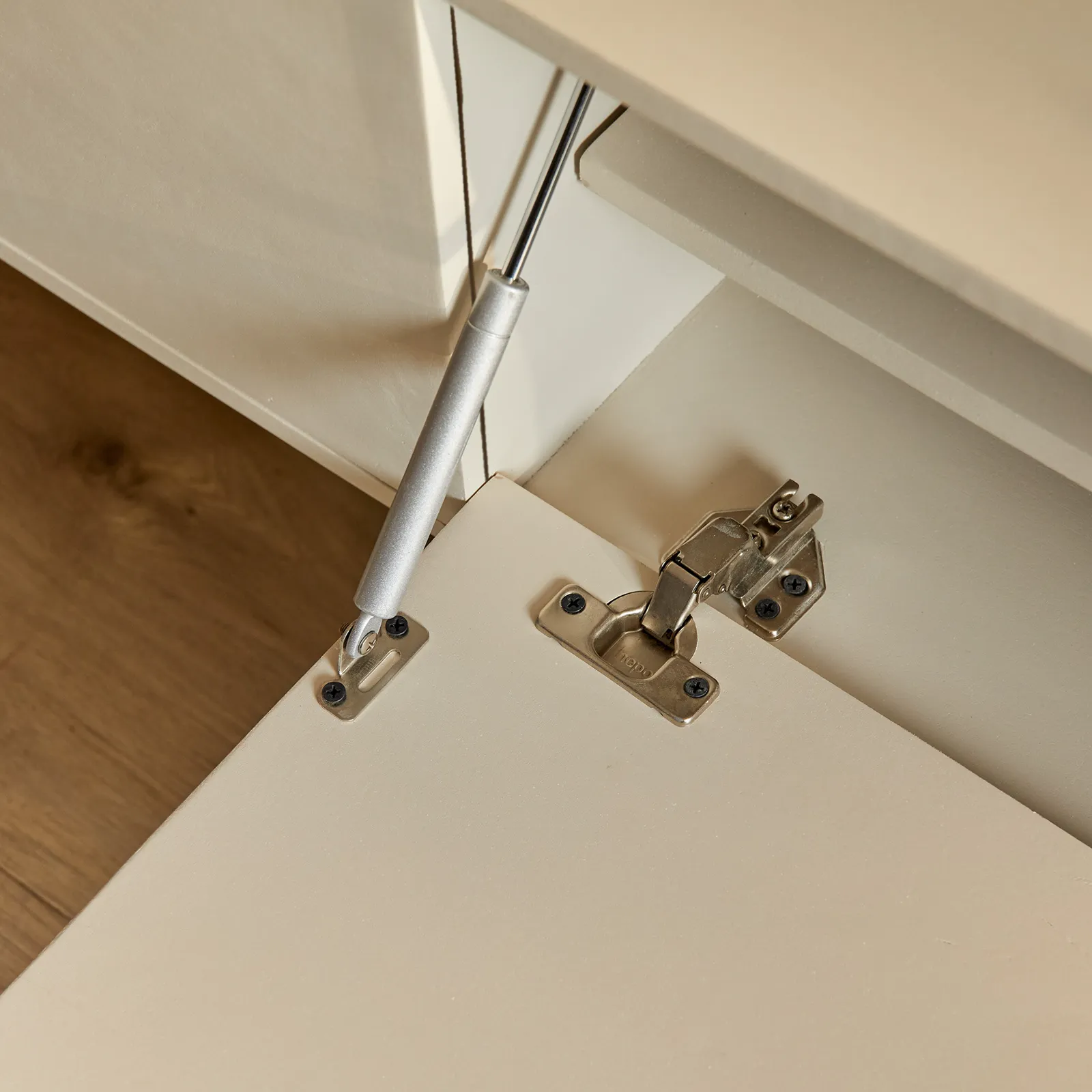 Detailopname van de scharnieren en gasveer van het zwevende tv meubel Vision Sand, met een houten vloer op de achtergrond - Starfurn