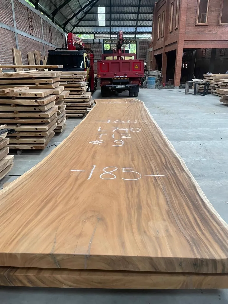 Baumstammplatte Bali Suarholz 7,4 Meter in einem Lagerraum mit einem roten LKW im Hintergrund - World of Brosi