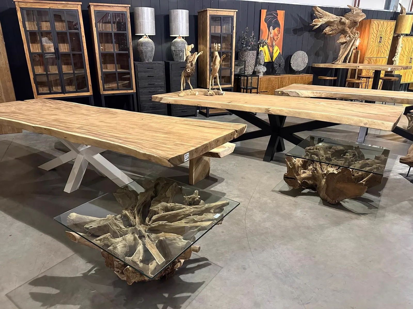Baumstammtisch Suarholz mit Spinnenbein in einem Möbel-Showroom, mit weiteren Tischen und Schränken im Hintergrund - World of Brosi