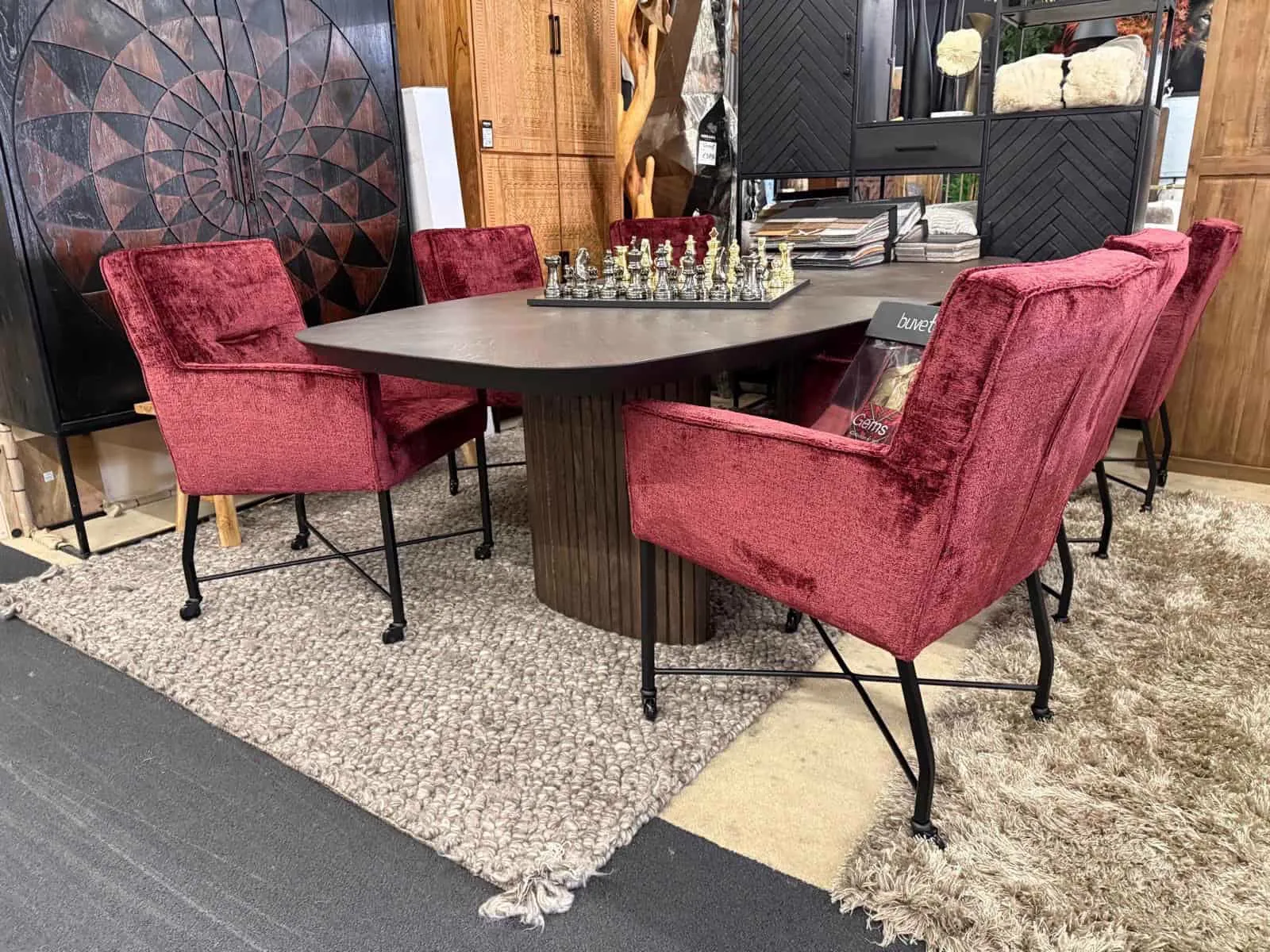 Sechs rote Esszimmerstühle Pesara mit Rollen um einen dunklen Esstisch, auf einem Hochflorteppich - Lenselink Furniture