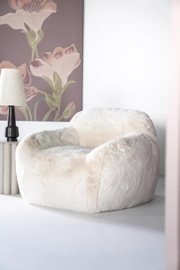 Der beige Hug Sessel in einem hellen Wohnzimmer mit einer Lampe und einem Blumengemälde - By-Boo