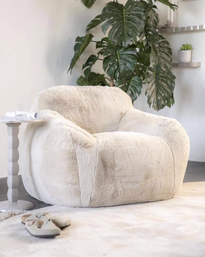 Der Sessel Hug - beige in einem hellen Wohnzimmer mit Pflanzen und einem Beistelltisch - By-Boo