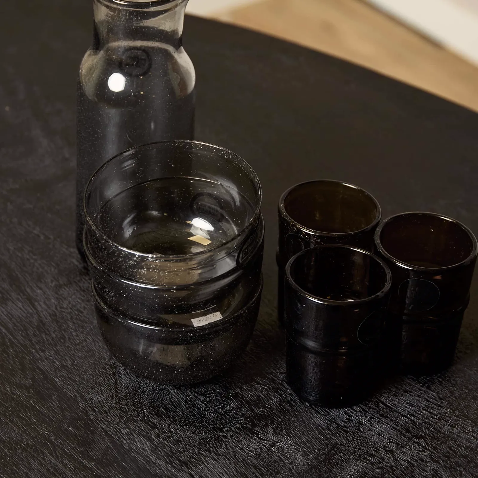 Eine Nahaufnahme einer schwarzen Karaffe und vier Gläser auf einem dunklen Holzhintergrund, mit dem Esstisch Brandy Black im Hintergrund - Starfurn