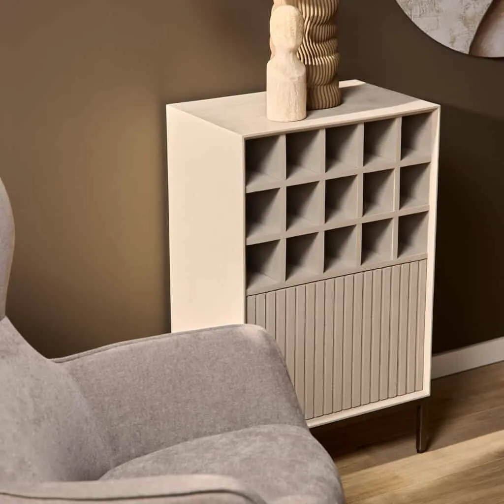Weinschrank Madison Sand mit offenen Fächern und vertikalen Lamellen, stehend in einem modernen Wohnzimmer neben einem grauen Sessel - Starfurn